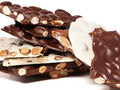Thin sheets of almond bark are shown in milk, dark or white chocolate. The sheets are broken into pieces, exposing the toasted almonds inside.