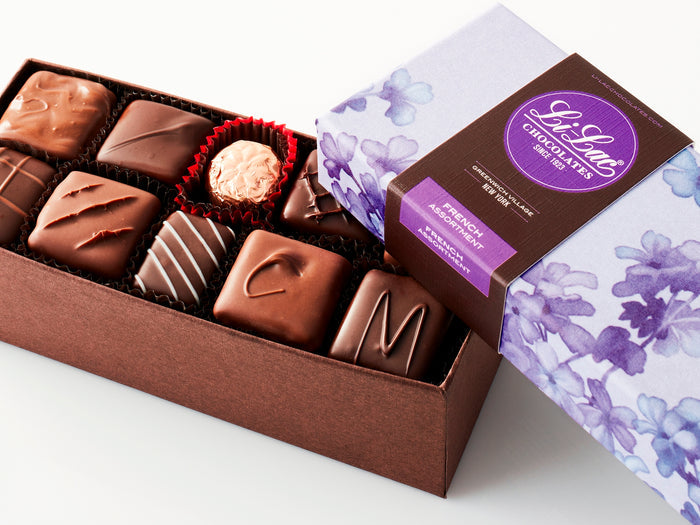 A large rectangular box of chocolate with a brown base and a purple lid with watercolor lilac motifs.