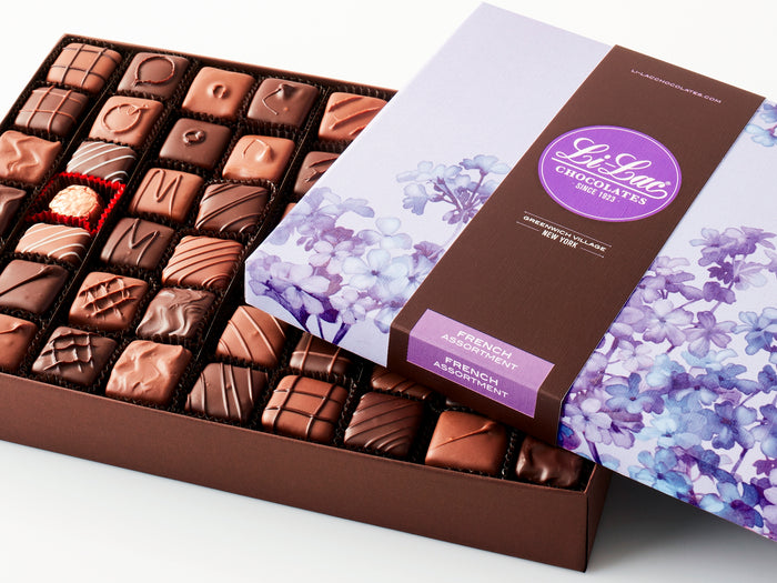 A large rectangular box of chocolate with a brown base and a purple lid with watercolor lilac motifs.