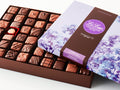 A large rectangular box of chocolate with a brown base and a purple lid with watercolor lilac motifs.