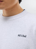A close-up of the '90's Dad' embroidery on the chest of the athletic grey sweatshirt from Percival.