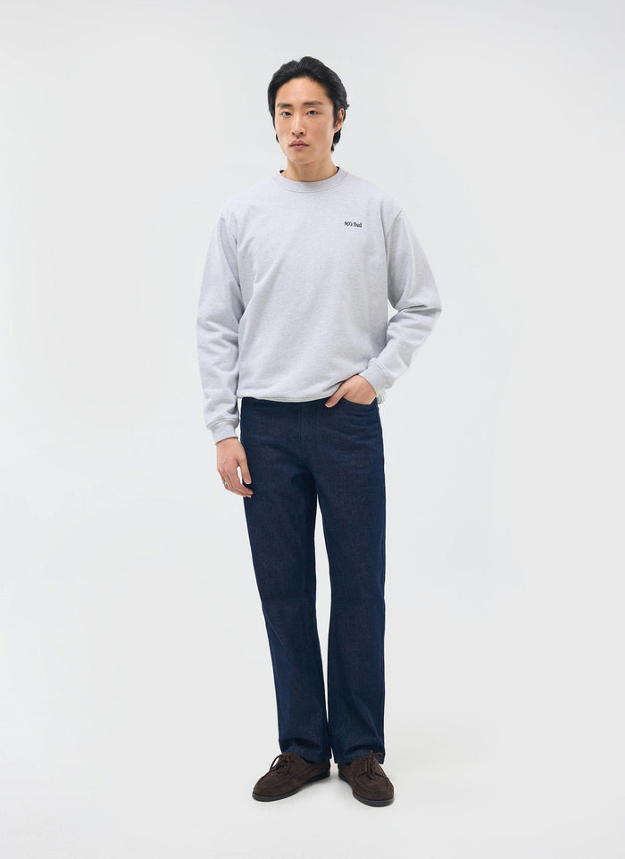 A model wears the Percival 90's Dad Sweatshirt in athletic grey with dark denim jeans against a white studio background.