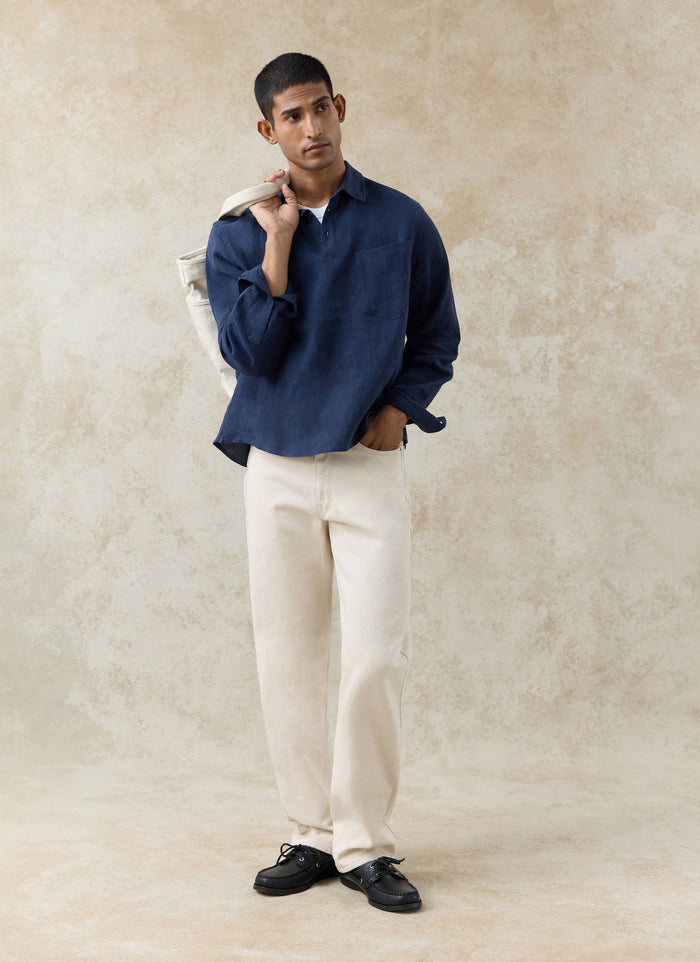 The Percival Alec Pullover Cropped Shirt in navy linen, with a half-placket and boxy fit, worn by a model in cream trousers.