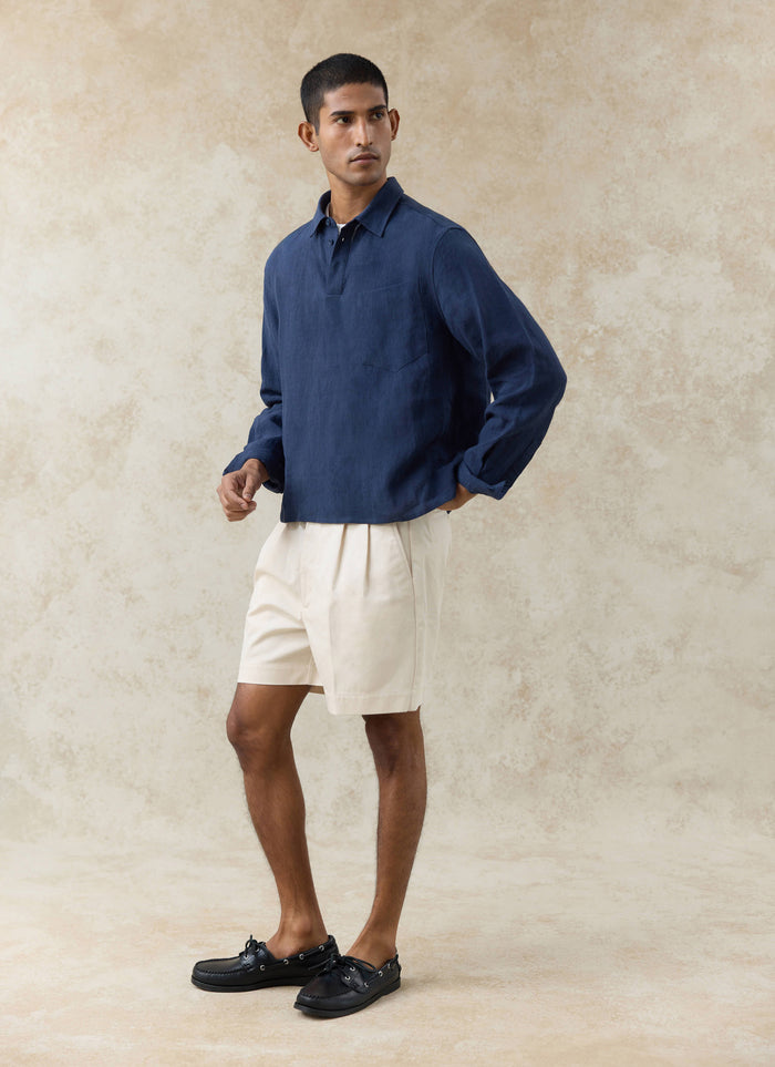 The Percival Alec Pullover Cropped Shirt in navy linen, a boxy style worn with cream shorts and black deck shoes.