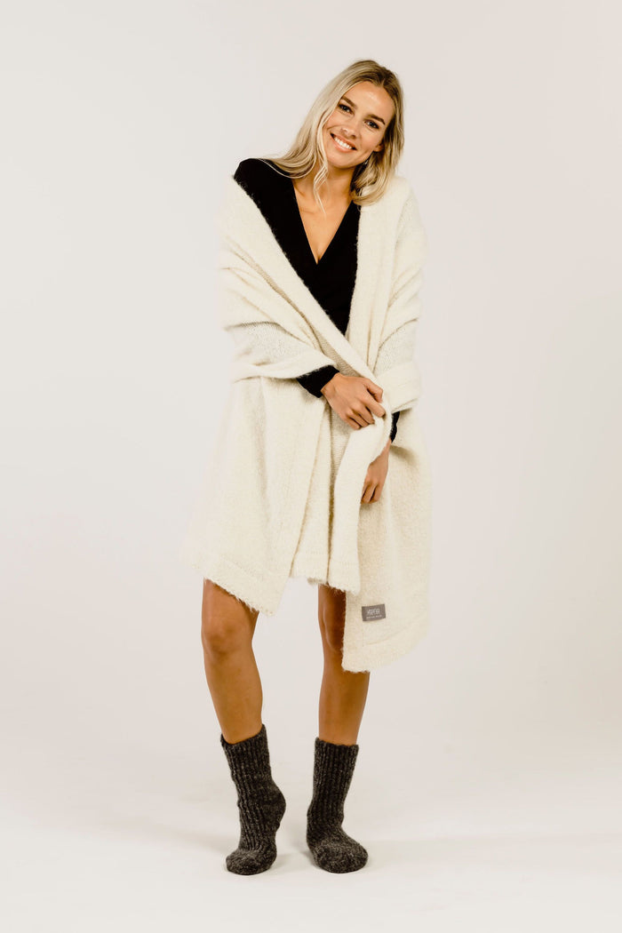 Woman wearing a cream-colored stole over her shoulders  and grey socks on a white background