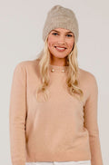 Woman wearing a pink sweater and knit beanie on a plain background