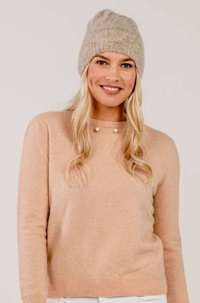 Woman wearing a pink sweater and knit beanie on a plain background