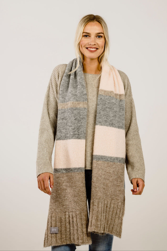 Woman wearing a beige sweater with a scarf on a plain background