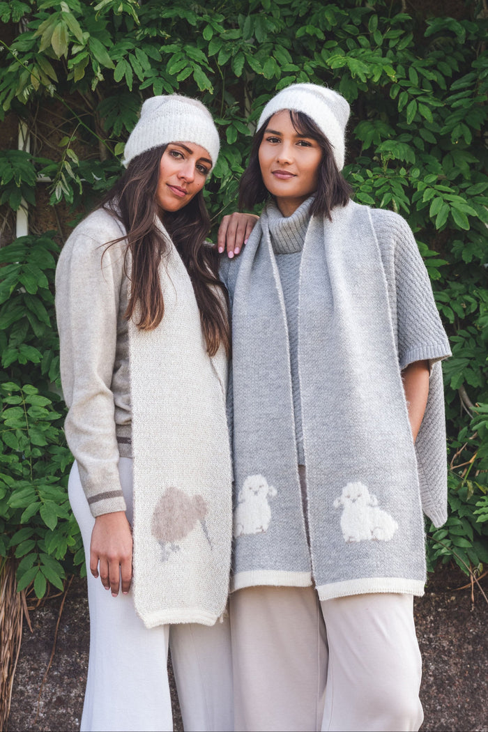 Two women wearing beanies and scarves with animal patterns standing in front of a green leafy background