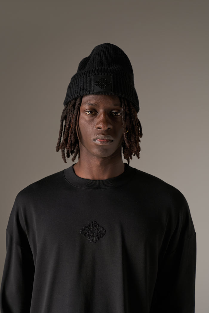 Man in a long sleeved black t-shirt and a beanie against a neutral background
