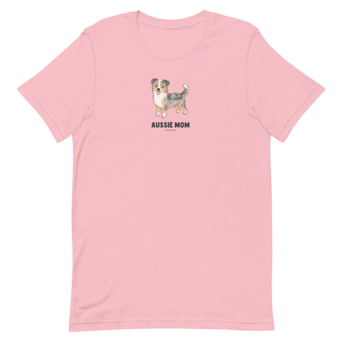 The Aussie Mom Tee by Sassy Woof is a light pink unisex shirt with an illustrated Australian Shepherd and bold black lettering, made from eco-friendly cotton—perfect for stylish, proud dog parents.