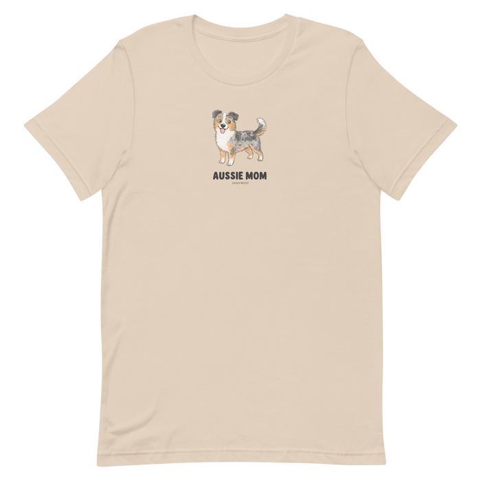 The Sassy Woof Aussie Mom Tee is a beige unisex shirt with an Australian Shepherd illustration above bold text, made from soft, eco-friendly cotton for comfort and style.