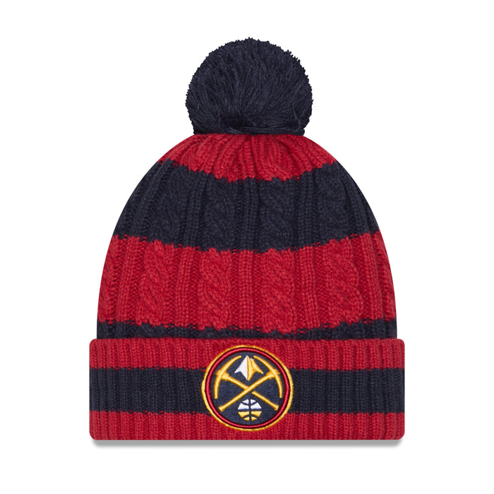 Front view of a thick winter knit pom beanie featuring horizontal stripes in dark navy blue and deep red. The body of the hat has a thick cable-knit texture, topped with a solid navy blue yarn pom-pom. The wide, ribbed cuff at the bottom mirrors the navy and red stripe pattern and features a prominent embroidered circular Denver Nuggets logo patch centered on the front