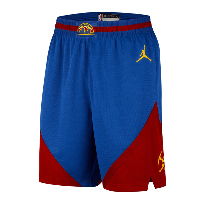 Front view of royal blue Denver Nuggets Statement Edition athletic shorts. The elastic waistband is royal blue with a thin horizontal dark red stripe running through it and a small gold, blue, and red mountain silhouette logo centered on the front buckle area. A gold Jordan Jumpman logo is embroidered on the left thigh. The bottom corners of both legs feature sharp, angled dark red geometric color-blocking that mimics mountain peaks, with a small gold crossed-pickaxes graphic printed on the lowe