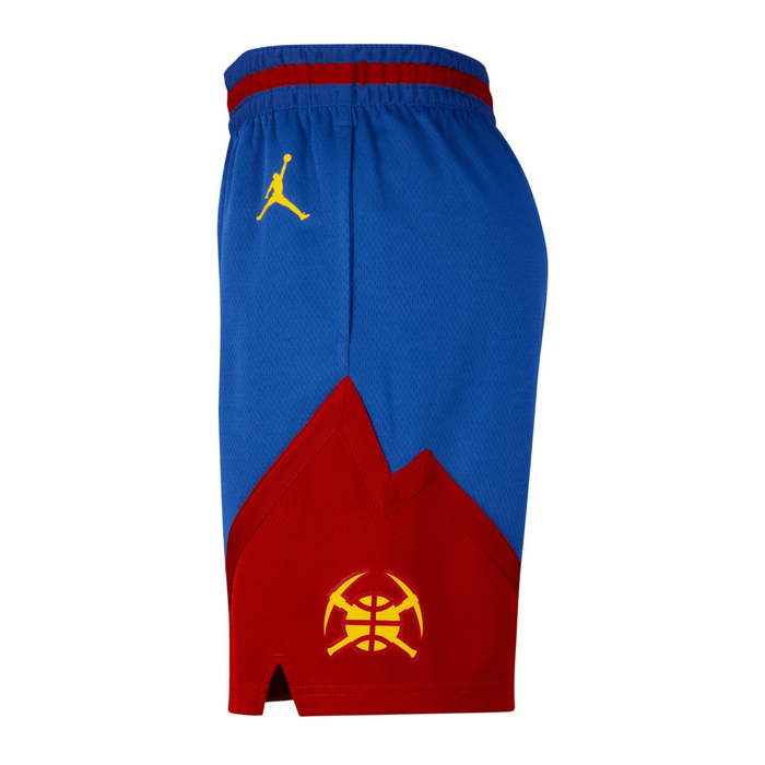 Left side view of the royal blue Denver Nuggets basketball shorts. The profile view showcases the elastic waistband with its integrated red stripe and highlights the dynamic, sharp mountain-peak silhouette of the red paneling along the side hem. A bright gold crossed-pickaxes team emblem is prominently printed inside the red graphic section near the vented lower slit