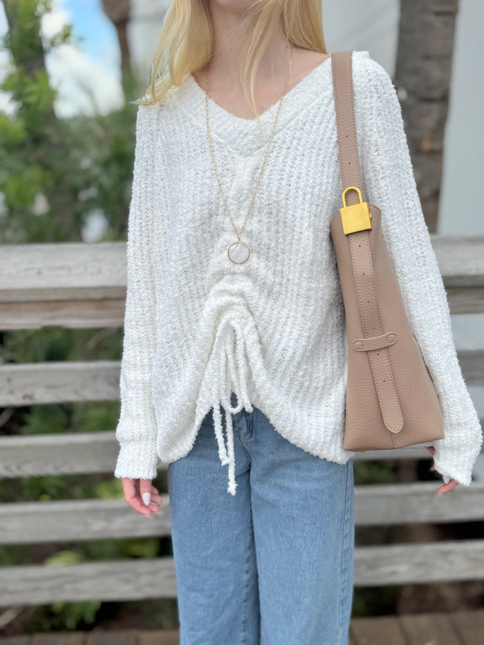 Person wearing a white knitted sweater and blue jeans, holding a beige handbag.