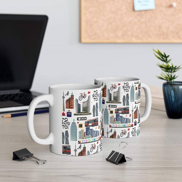 Two mugs with Toronto-themed designs on a desk with office supplies.