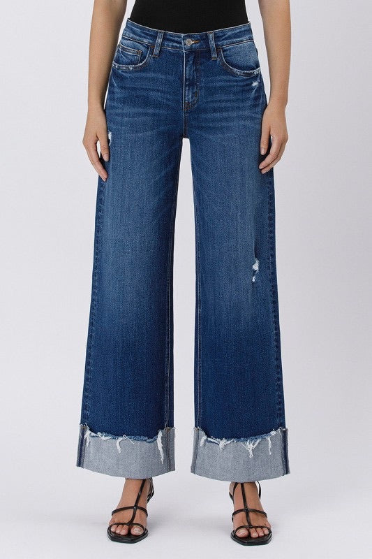 Model wearing high rise cuffed baggy wide leg jeans with slight distressing and raw single cuff hem, styled with black heels and a fitted black tank top (front view).