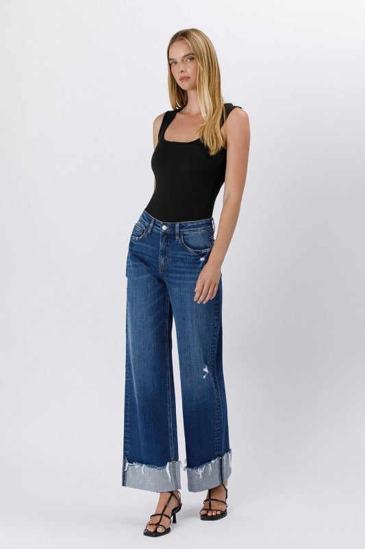 Model wearing high rise cuffed baggy wide leg jeans with slight distressing and raw single cuff hem, styled with black heels and a fitted black tank top (front view).
