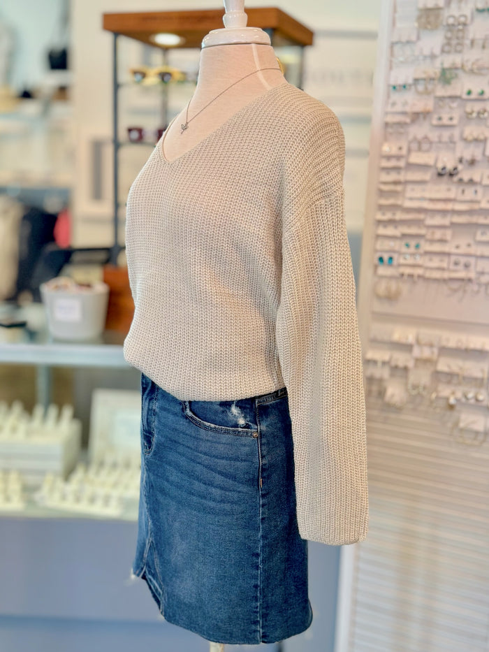 Mannequin wearing a beige sweater and blue jean skirt in an indoor setting