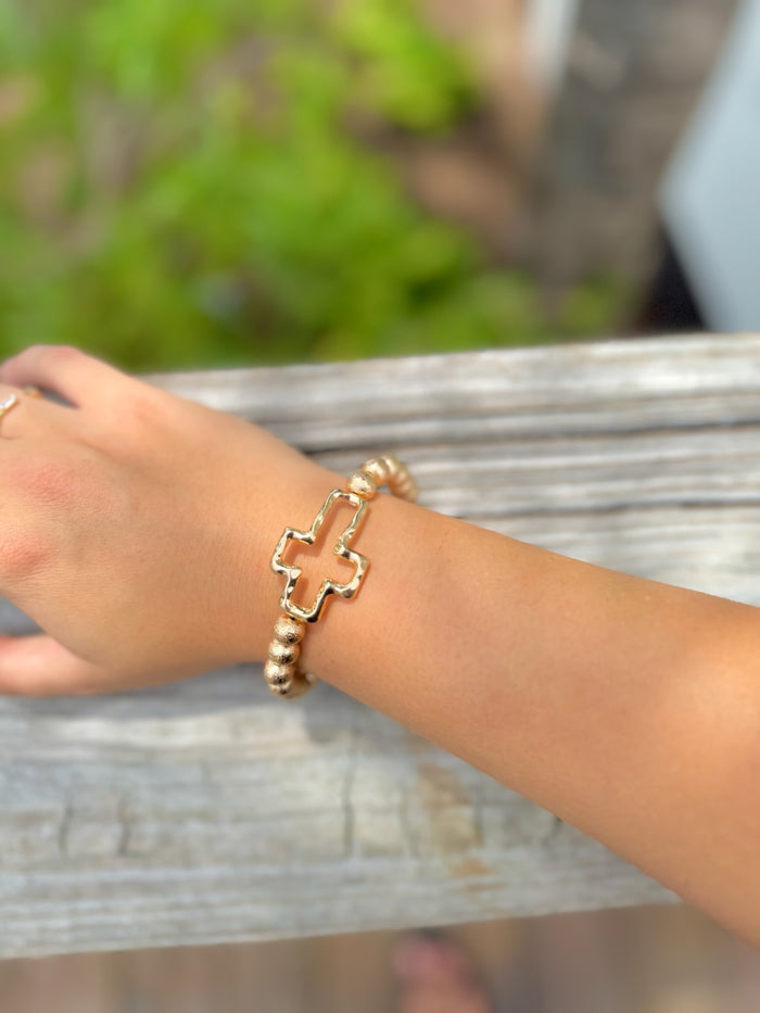Gold beaded stretch bracelet with polished cross charm on woman's arm
