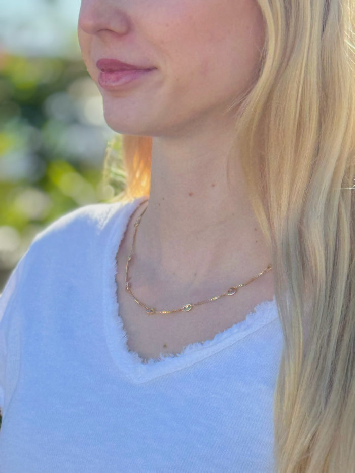 Close-up of a person wearing a gold necklace with a blurred natural background