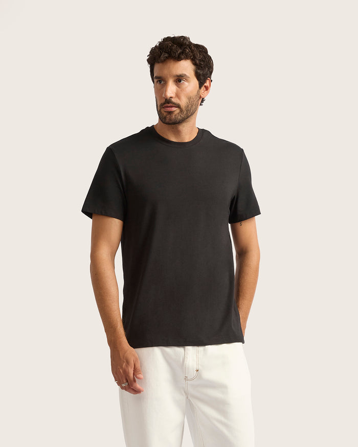Man wearing a black t-shirt and white pants against a plain background