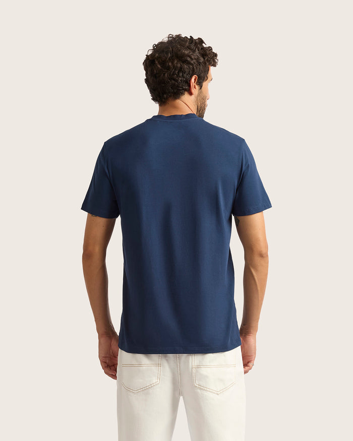 Man wearing a navy blue t-shirt and white pants on a light beige background