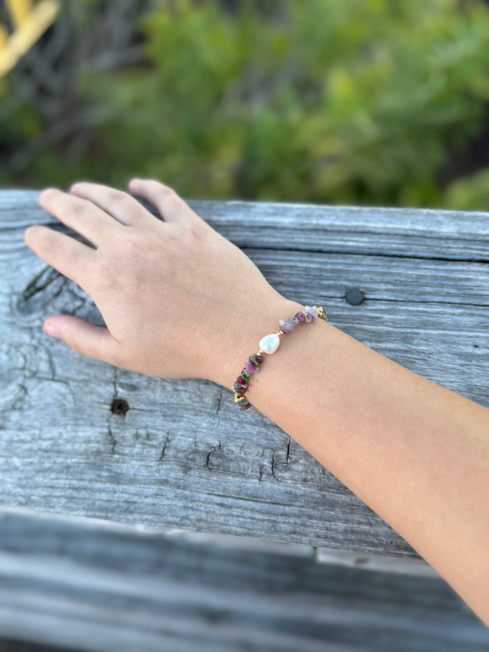 Hand wearing a beaded bracelet on a wooden surface with greenery in the background