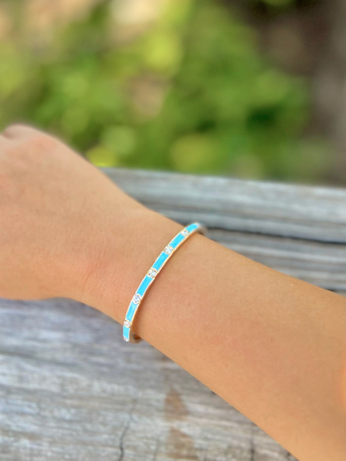 Gold bracelet with turquoise band and sparkle accents on a wrist with blurred background.