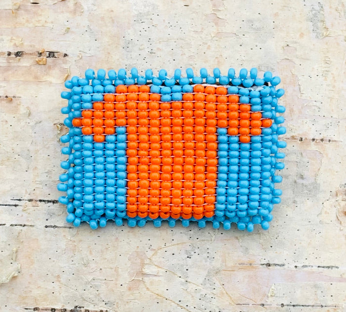 Beaded rectangular pin with orange shirt on a birch bark background