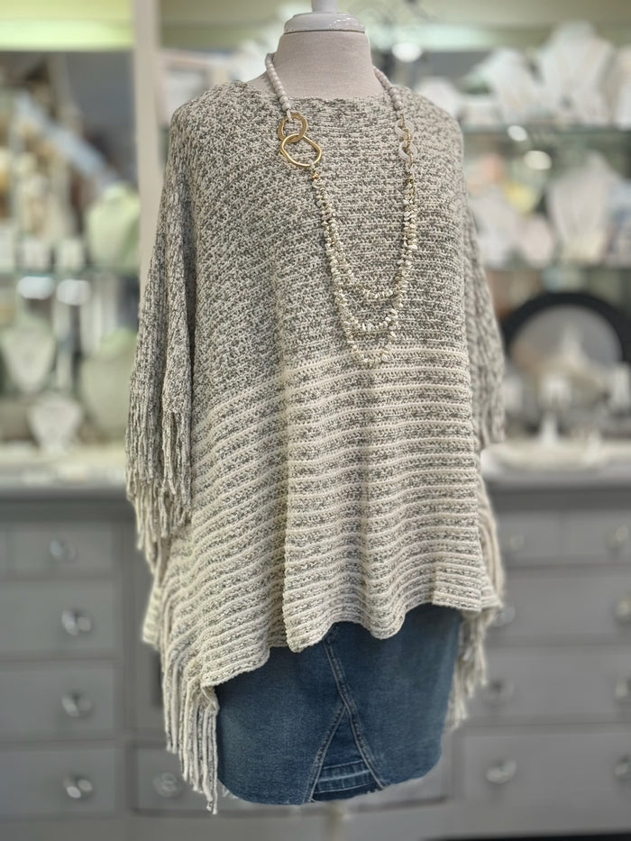 Knitted poncho on a mannequin in front of a store display.