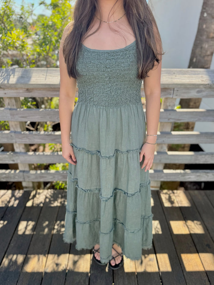 Woman wearing a green tiered dress standing on a wooden deck with blurred background