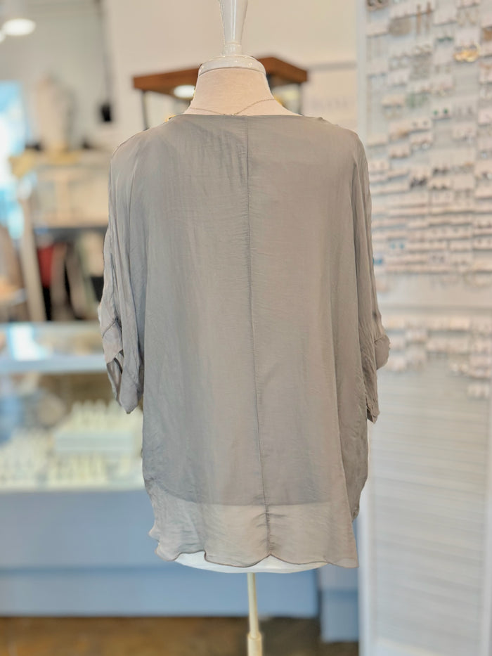 Light gray blouse on a mannequin against a blurred indoor background