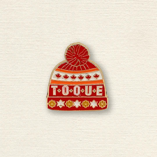 Pin of a red toque with 'TOQUE' text on a textured beige background