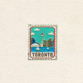 Enamel pin with Toronto skyline design on a textured beige background