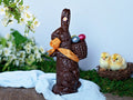 a large chocolate bunny carrying a basket on his back with three foiled eggs.
